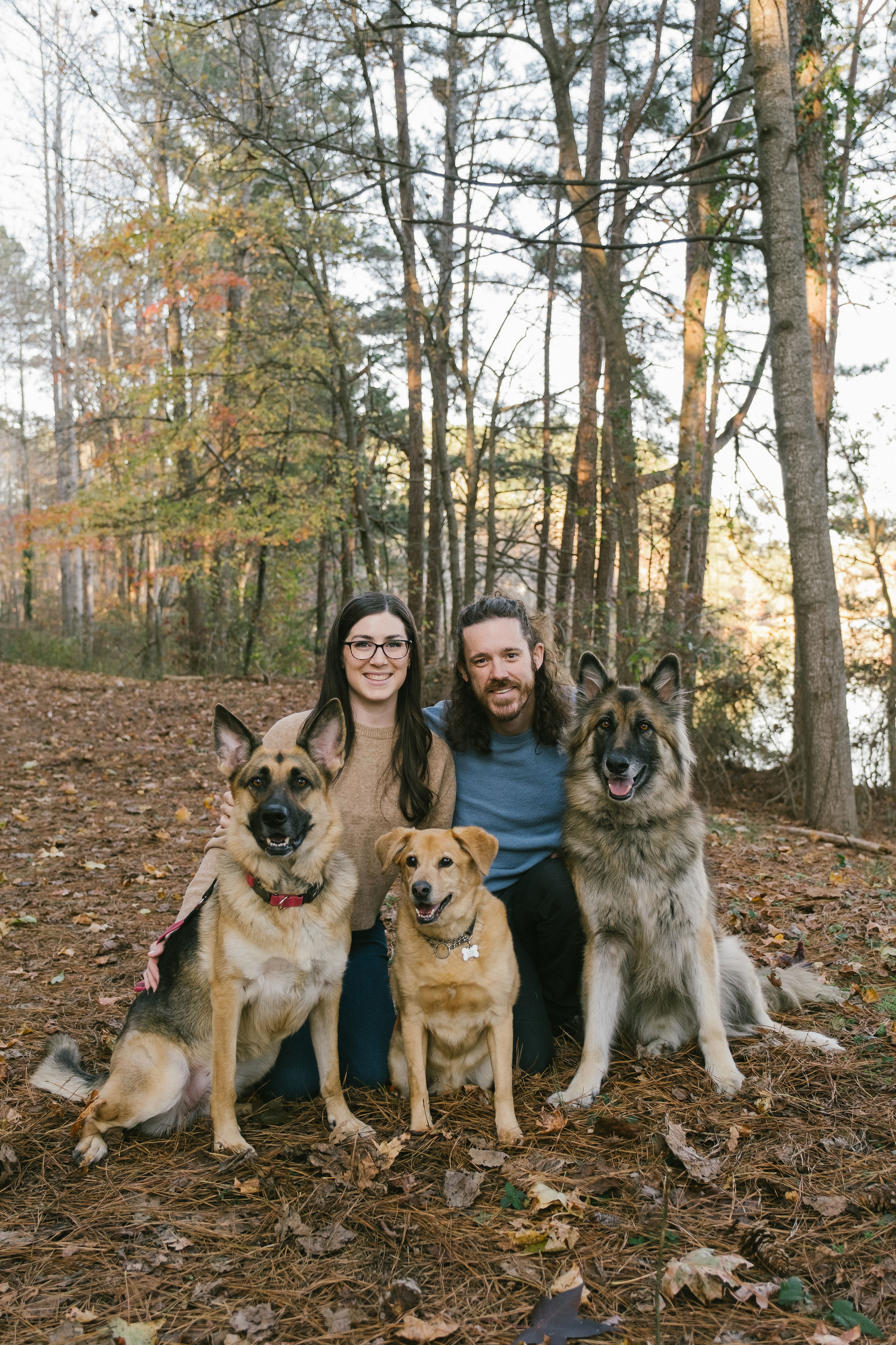 A smiling couple kneeling with their three dogs in the woods