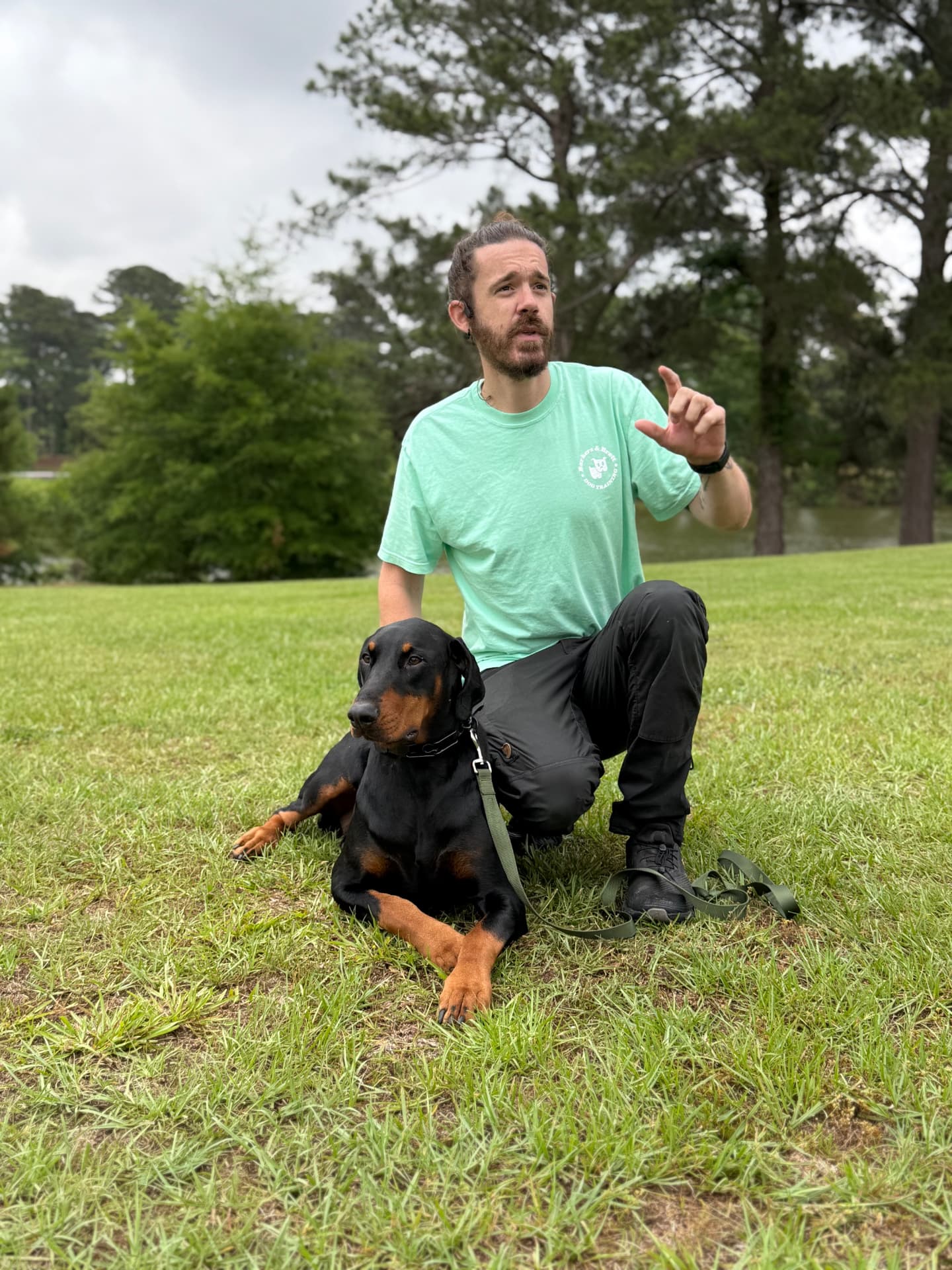 Brett working with a Doberman holding a down-stay in a grass field